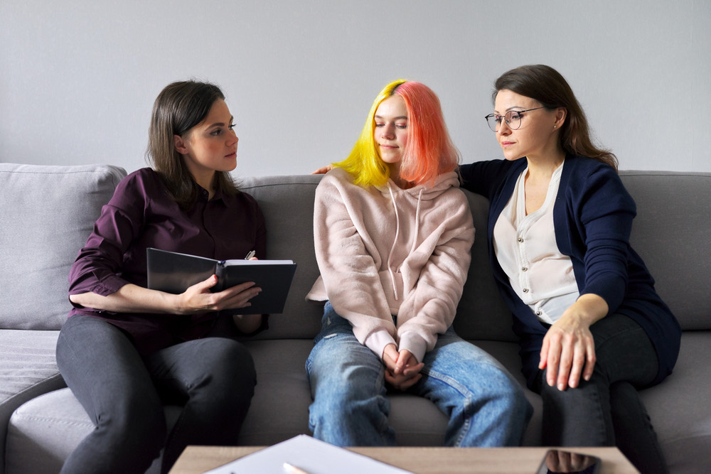 A teen and a parent sitting on a couch with a counselor